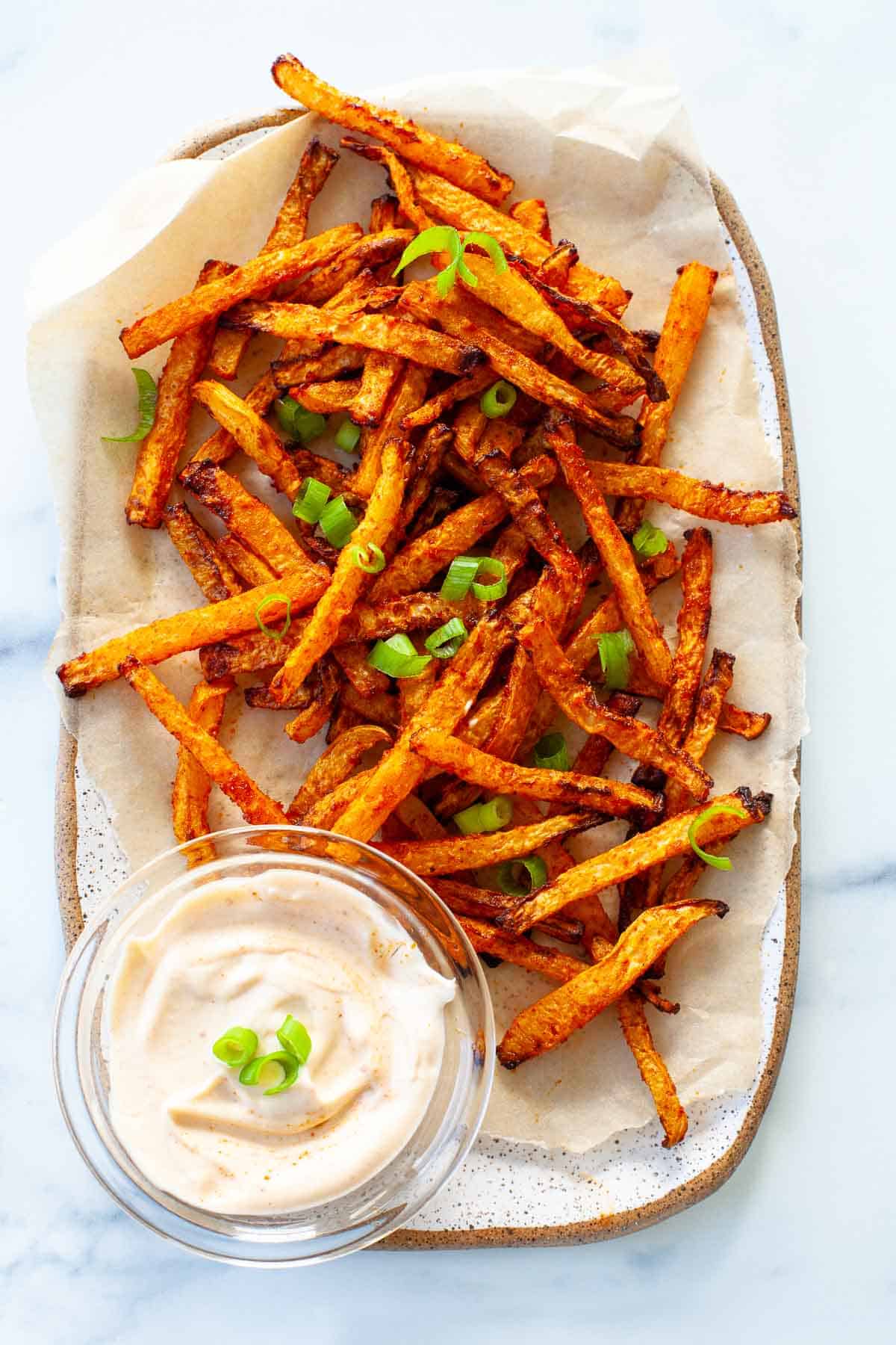 crispy kohlrabi fries. scallion garnish. on large white speckled plate. glass bowl of dip. 