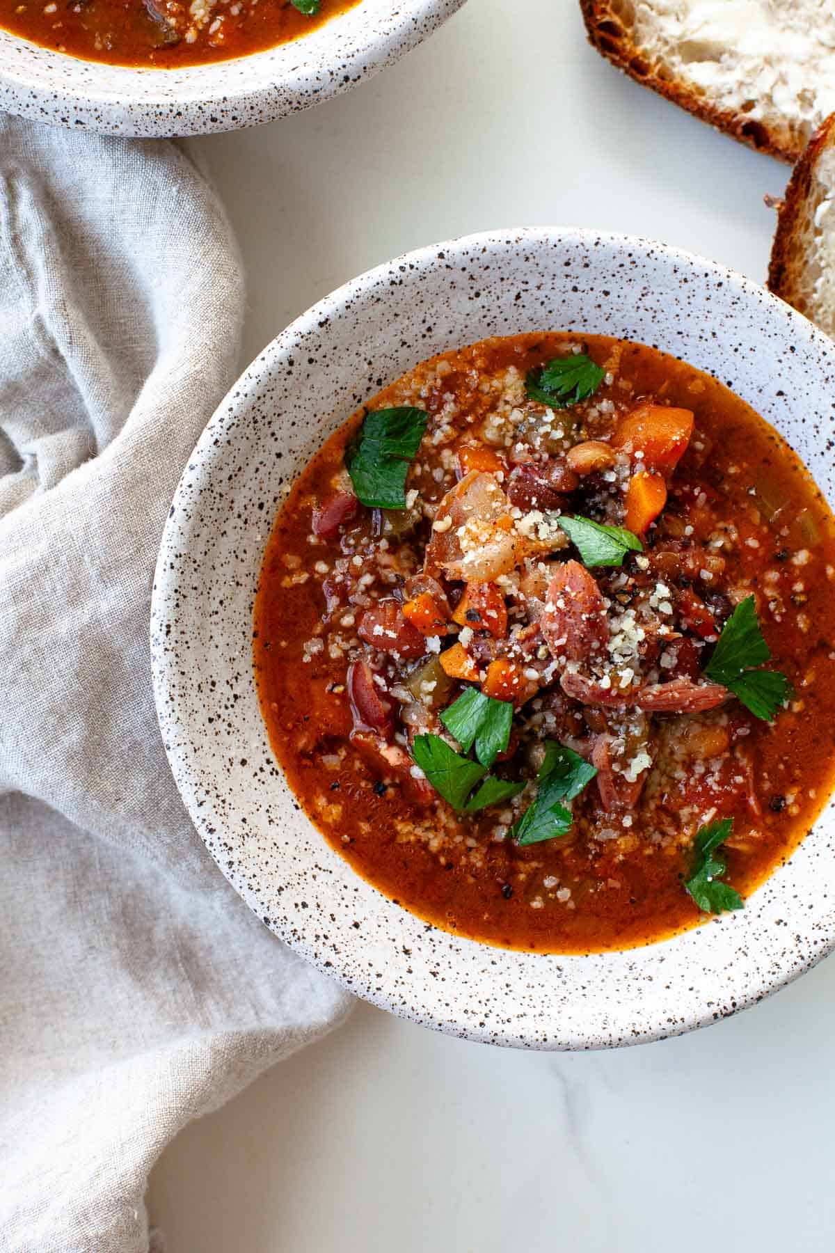 Instant Pot 15 Bean Soup served in a white speckled bowl garnished with freshly cracked black pepper, parmesan cheese and parsley.