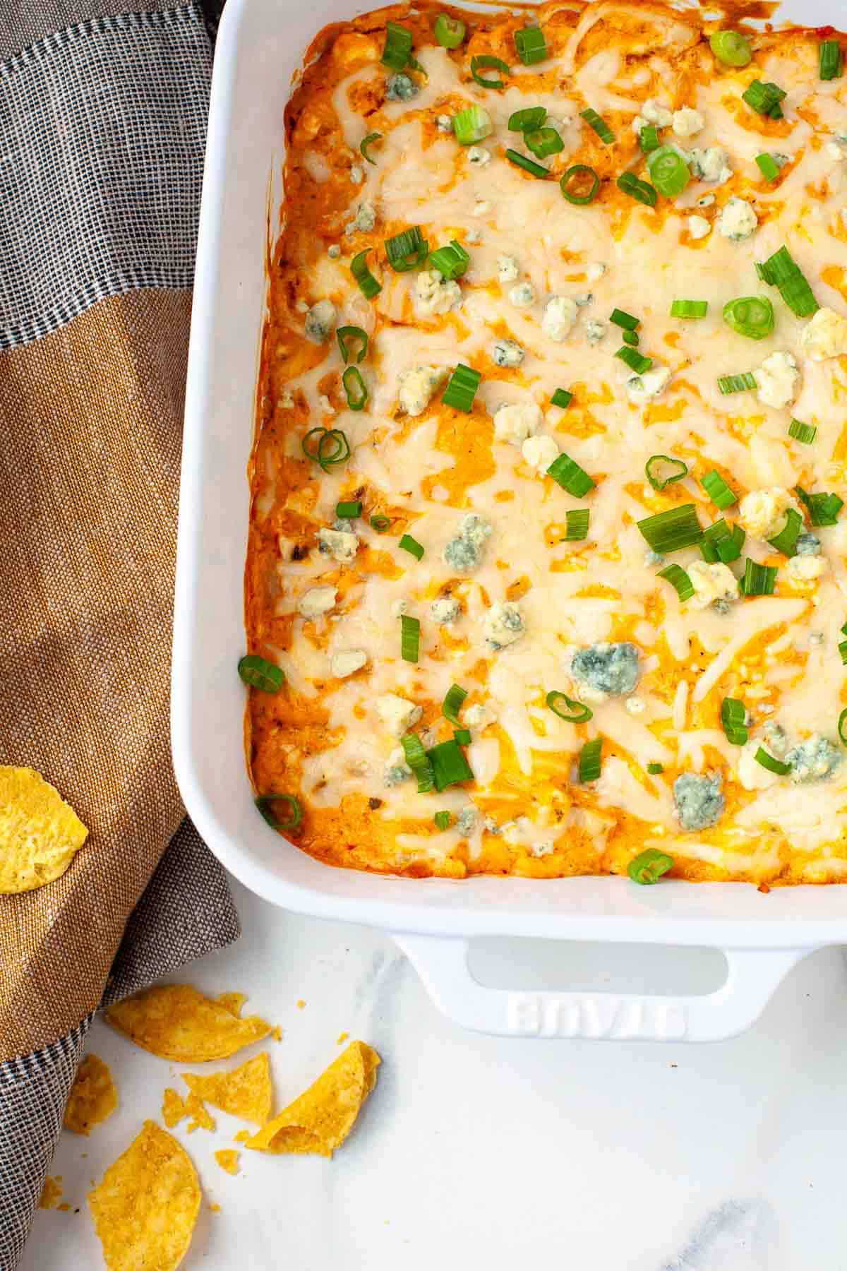 Buffalo Cauliflower Dip in white baking dish beside kitchen towel and a few tortilla chips