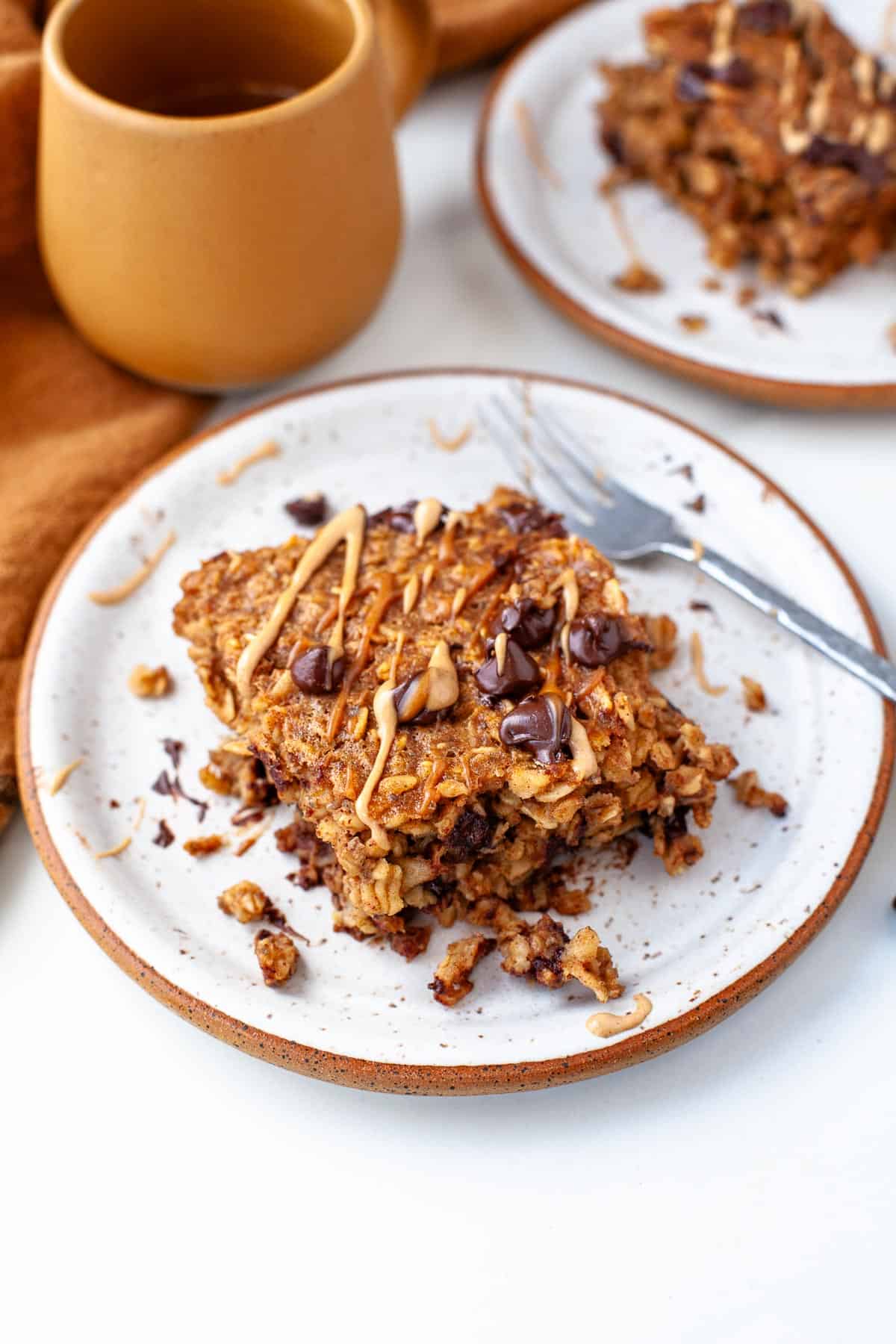 serving of peanut butter baked oatmeal on white speckled plate topped with chocolate chips and a drizzle of peanut butter.