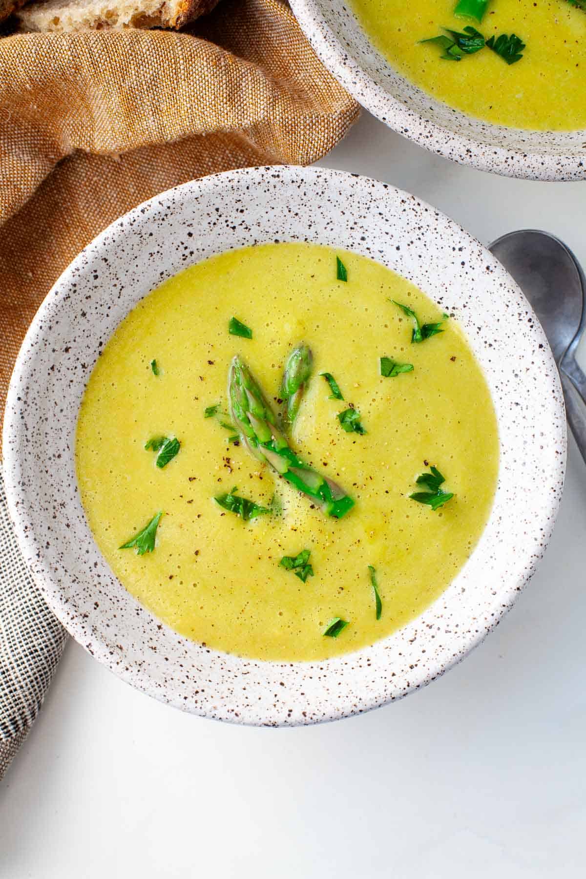 bowl of vegan asparagus soup garnished with two pieces of chopped asparagus and freshly chopped parsley.