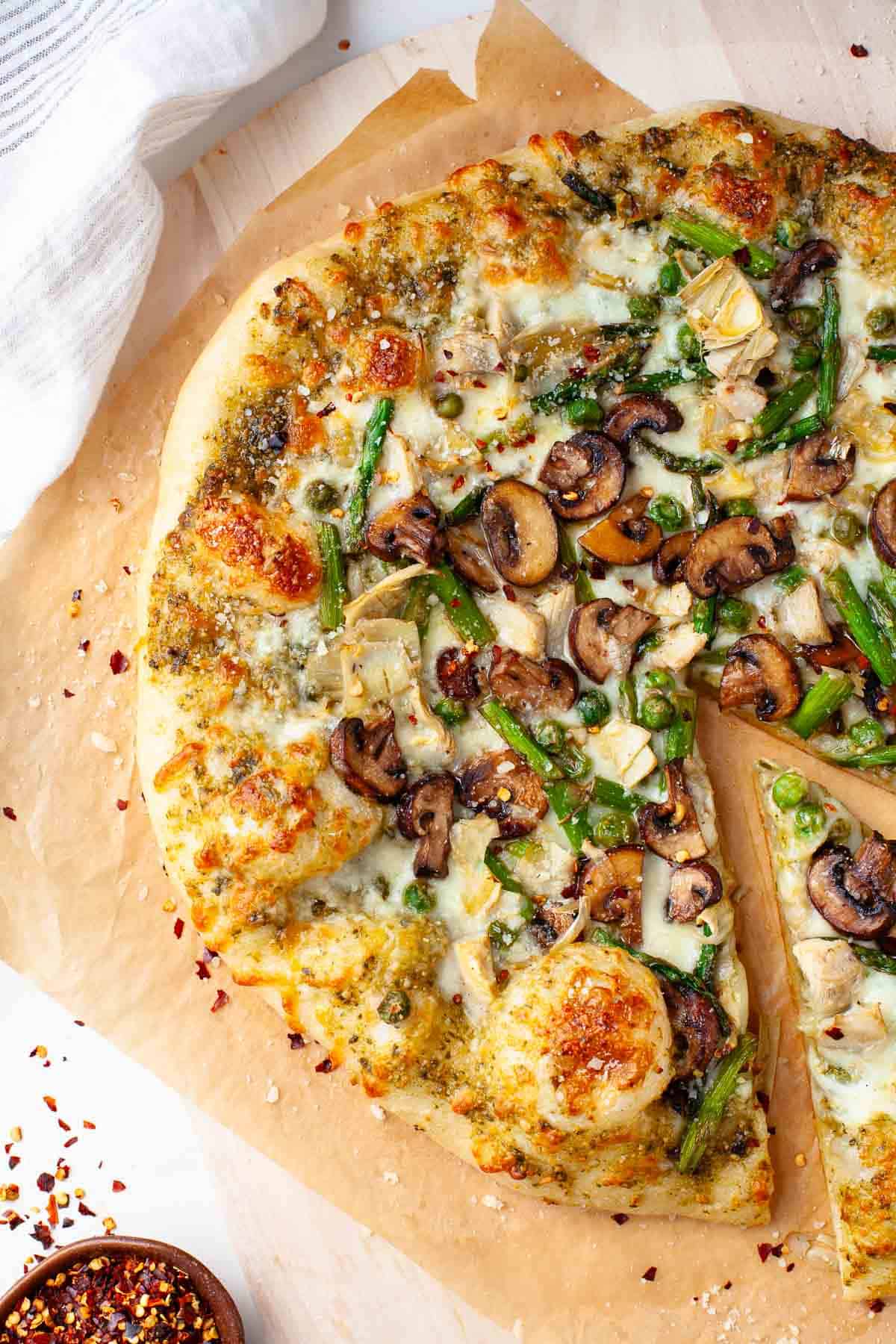 spring pizza garnished with grated parmesan cheese and red pepper flakes on top of pizza stone.